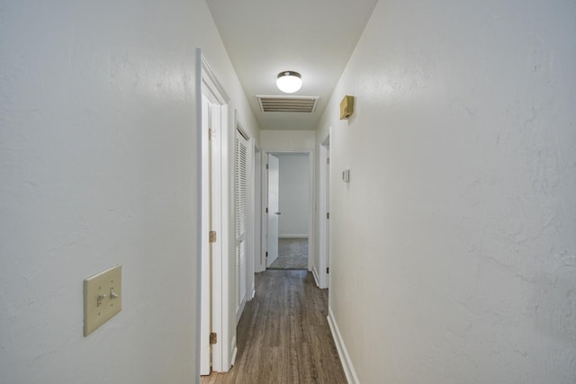 hallway featuring visible vents, baseboards, and wood finished floors