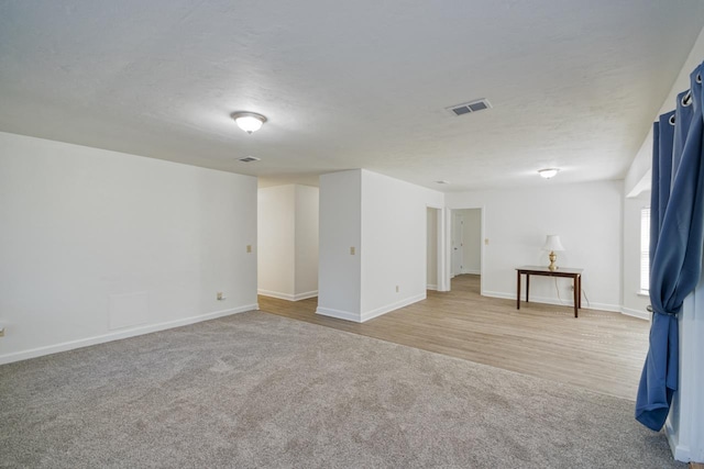 unfurnished room with baseboards, visible vents, light carpet, and a textured ceiling