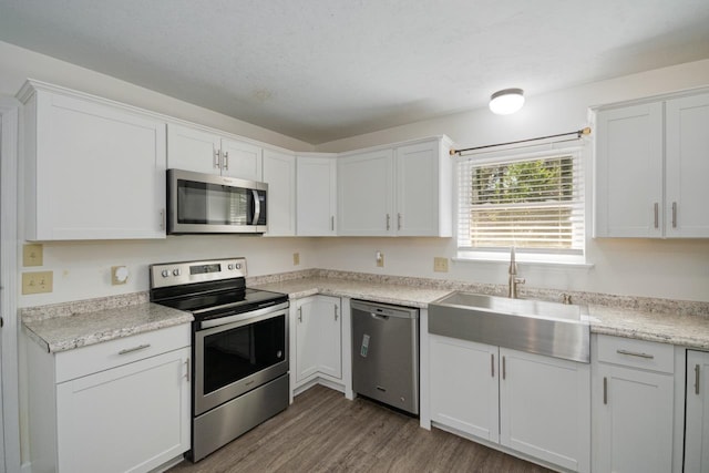 kitchen with stainless steel appliances, a textured ceiling, light wood-type flooring, white cabinetry, and a sink