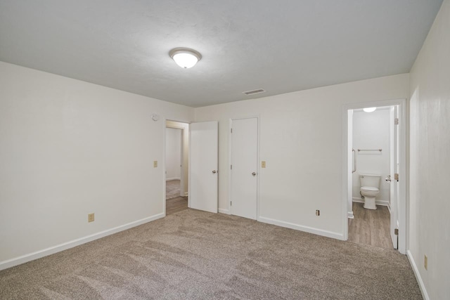 unfurnished bedroom with ensuite bath, baseboards, visible vents, and carpet flooring