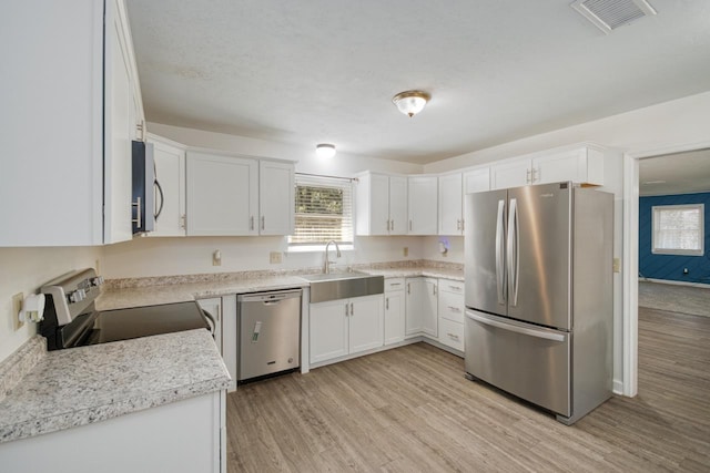 kitchen with stainless steel appliances, a sink, visible vents, white cabinets, and light wood finished floors