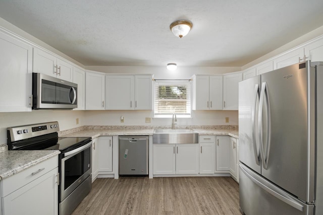 kitchen featuring light stone counters, stainless steel appliances, light wood-style flooring, white cabinetry, and a sink