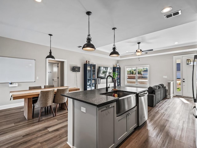 kitchen with gray cabinetry, a center island with sink, sink, stainless steel dishwasher, and dark hardwood / wood-style floors