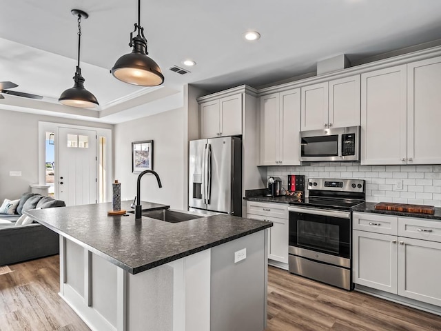 kitchen with appliances with stainless steel finishes, tasteful backsplash, sink, decorative light fixtures, and an island with sink