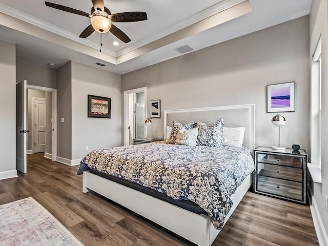 bedroom with ornamental molding, a tray ceiling, ceiling fan, and dark wood-type flooring