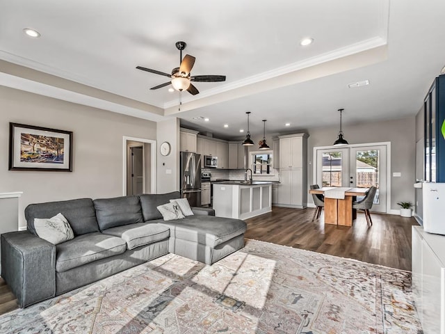 living room featuring ceiling fan, french doors, dark hardwood / wood-style flooring, a tray ceiling, and ornamental molding