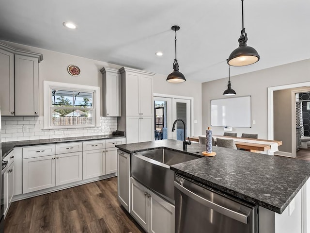 kitchen featuring dishwasher, a kitchen island with sink, sink, dark stone countertops, and decorative light fixtures