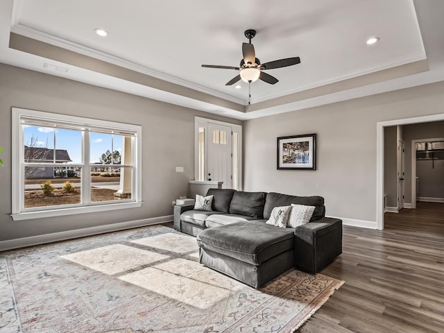 living room with a raised ceiling, ceiling fan, crown molding, and dark wood-type flooring