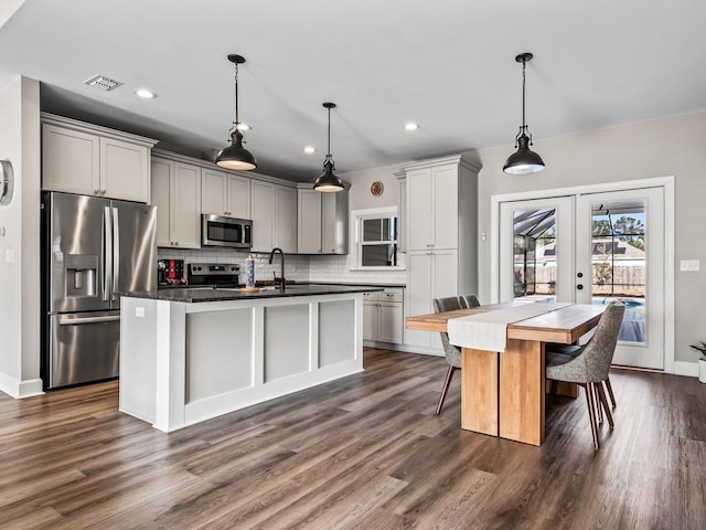 kitchen featuring french doors, stainless steel appliances, decorative light fixtures, gray cabinets, and a kitchen island with sink