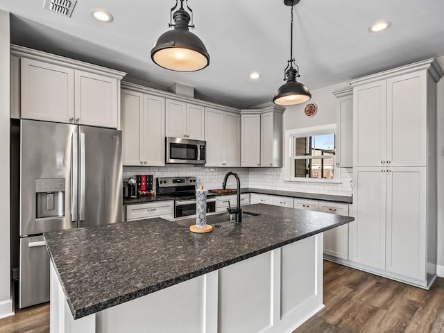 kitchen featuring stainless steel appliances, sink, decorative light fixtures, dark stone countertops, and an island with sink