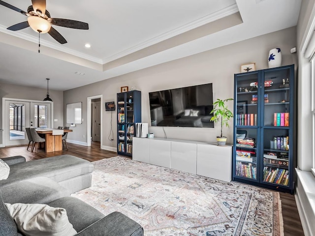 living room featuring dark hardwood / wood-style floors, a raised ceiling, ceiling fan, and crown molding