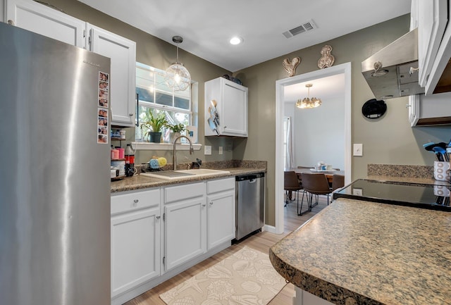 kitchen with appliances with stainless steel finishes, a sink, a chandelier, light wood finished floors, and white cabinetry
