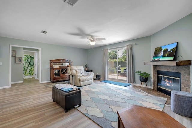 living area featuring light wood-style flooring, a ceiling fan, a tiled fireplace, and baseboards