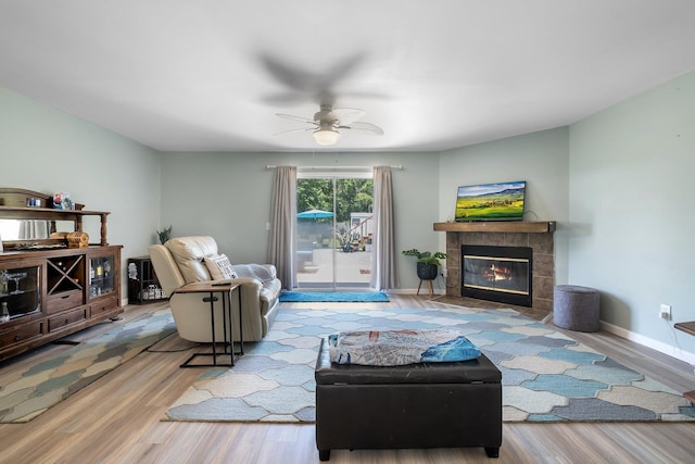 living room with wood finished floors, ceiling fan, a tiled fireplace, and baseboards