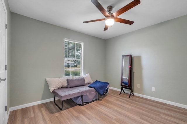 living area with light wood-style floors, a ceiling fan, and baseboards