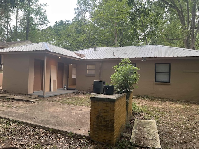 rear view of property with concrete block siding, central air condition unit, and metal roof