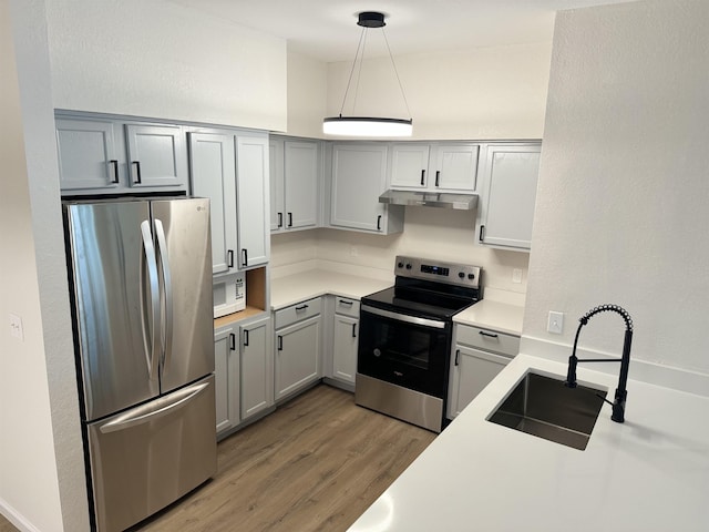 kitchen with appliances with stainless steel finishes, gray cabinetry, sink, decorative light fixtures, and hardwood / wood-style floors