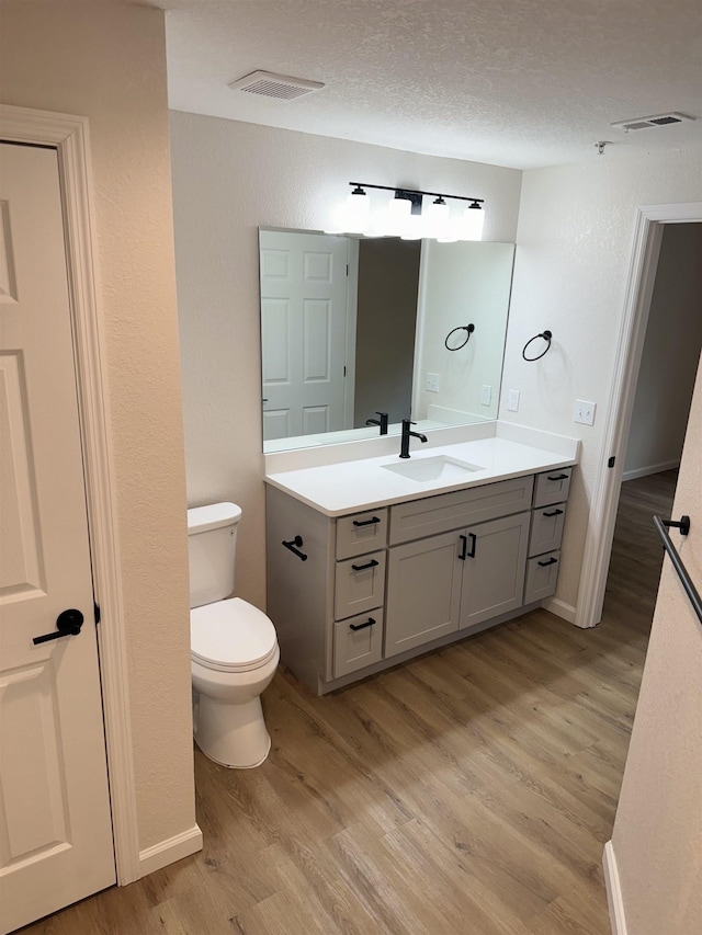 bathroom with vanity, a textured ceiling, hardwood / wood-style flooring, and toilet