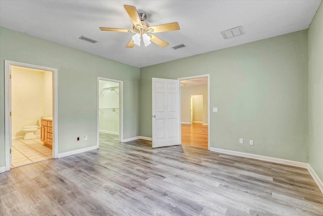 unfurnished bedroom featuring a spacious closet, ensuite bath, light hardwood / wood-style floors, and a closet