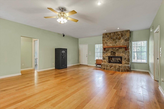 unfurnished living room with a stone fireplace, ceiling fan, and light wood-type flooring