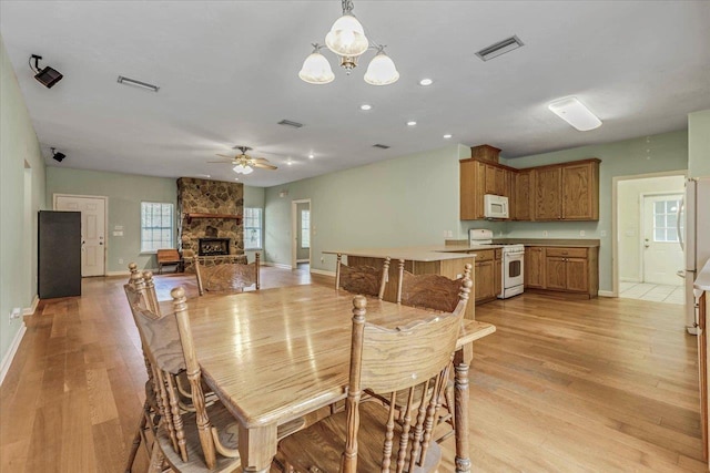 dining area featuring a stone fireplace, light hardwood / wood-style flooring, and ceiling fan with notable chandelier