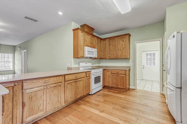 kitchen with white appliances, kitchen peninsula, and light wood-type flooring