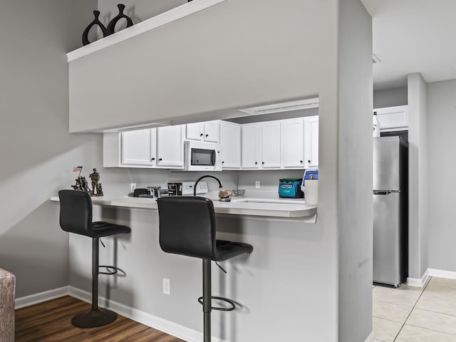 kitchen with white cabinets, light tile patterned floors, kitchen peninsula, stainless steel refrigerator, and a breakfast bar