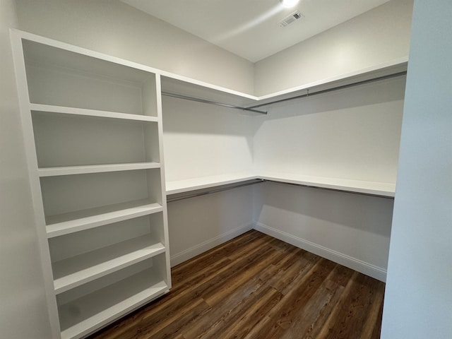 spacious closet featuring visible vents, dark wood-type flooring, and built in desk