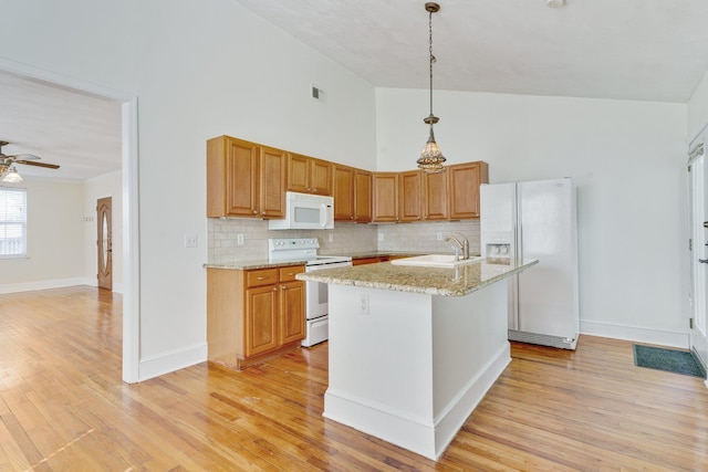 kitchen featuring light stone countertops, hanging light fixtures, tasteful backsplash, white appliances, and a kitchen island with sink