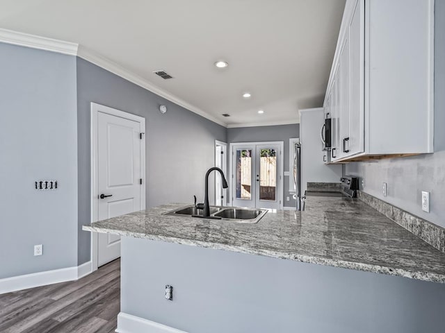 kitchen with appliances with stainless steel finishes, white cabinetry, sink, light stone counters, and kitchen peninsula