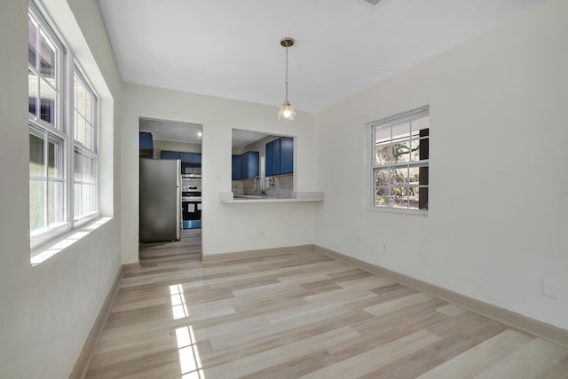 unfurnished dining area with a sink, baseboards, and light wood-style flooring