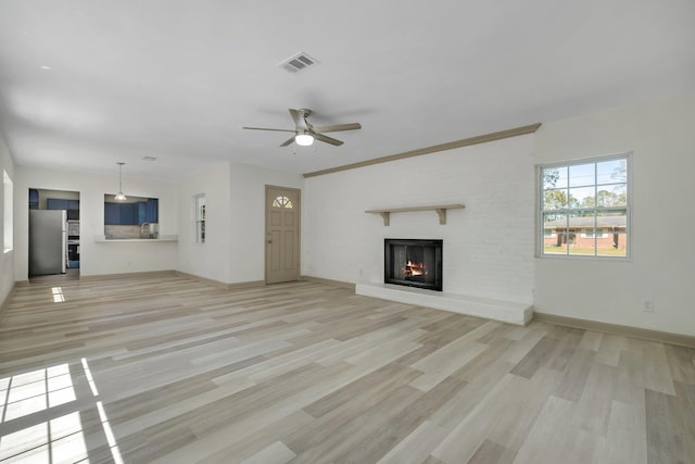 unfurnished living room featuring visible vents, baseboards, a warm lit fireplace, and light wood-style flooring