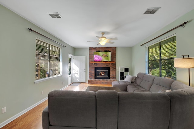 living room with ceiling fan, light wood-type flooring, a brick fireplace, and a wealth of natural light