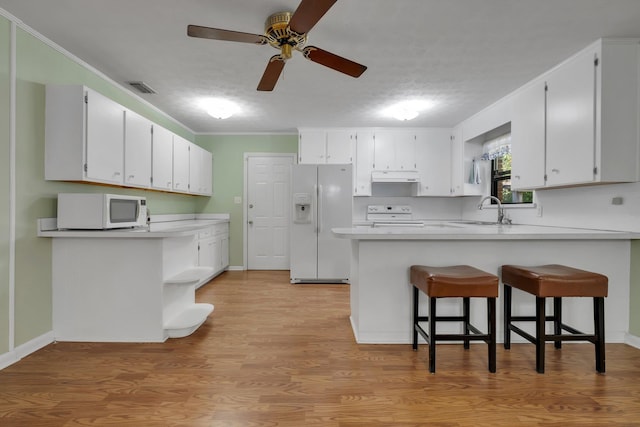 kitchen featuring white appliances, a kitchen breakfast bar, kitchen peninsula, and white cabinets