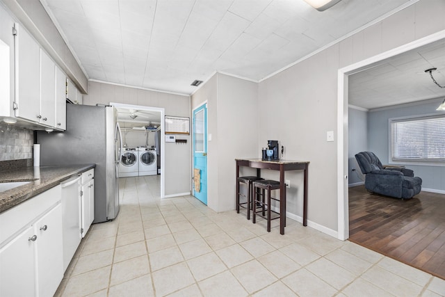 kitchen featuring white cabinetry, plenty of natural light, ornamental molding, and washing machine and clothes dryer