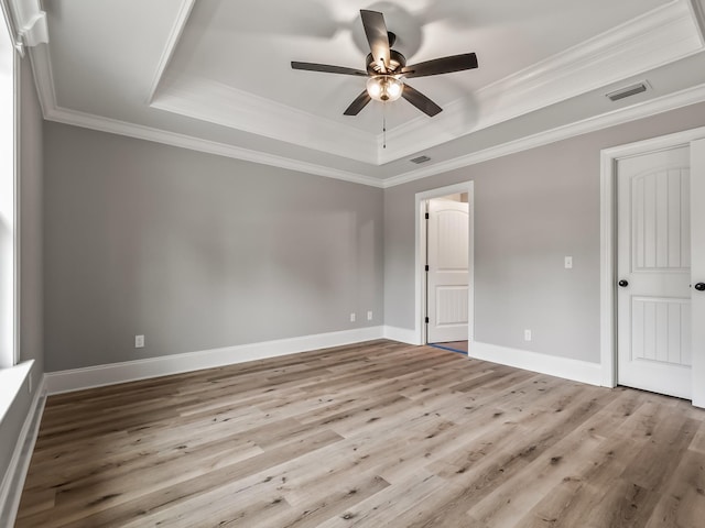 unfurnished bedroom featuring crown molding, visible vents, wood finished floors, and a tray ceiling
