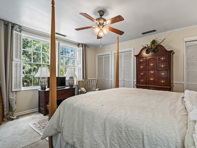 carpeted bedroom with ornamental molding, ceiling fan, and two closets