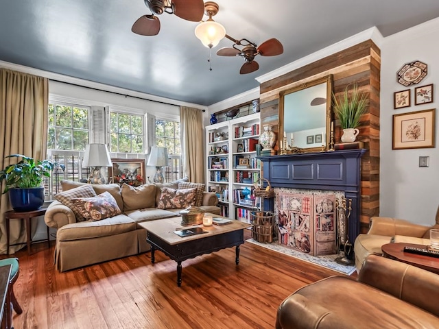 living room with built in shelves, wood-type flooring, ceiling fan, and crown molding