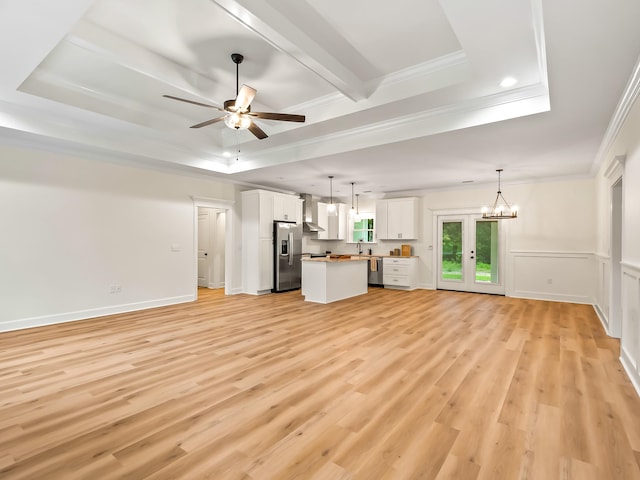 unfurnished living room with a tray ceiling, ceiling fan with notable chandelier, ornamental molding, and light hardwood / wood-style flooring