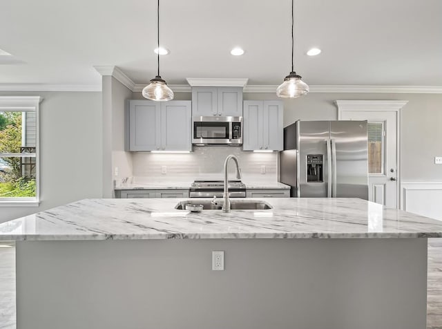 kitchen featuring light stone countertops, pendant lighting, stainless steel appliances, an island with sink, and sink