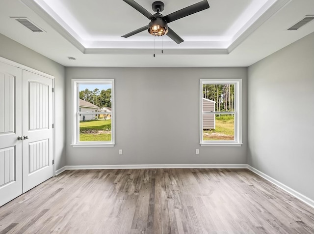 unfurnished bedroom featuring ceiling fan, a closet, light wood-type flooring, and a tray ceiling