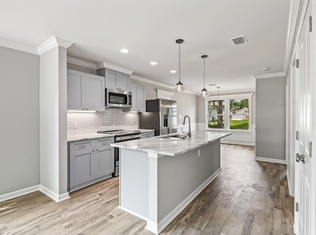 kitchen with light stone countertops, appliances with stainless steel finishes, gray cabinetry, sink, and a center island with sink