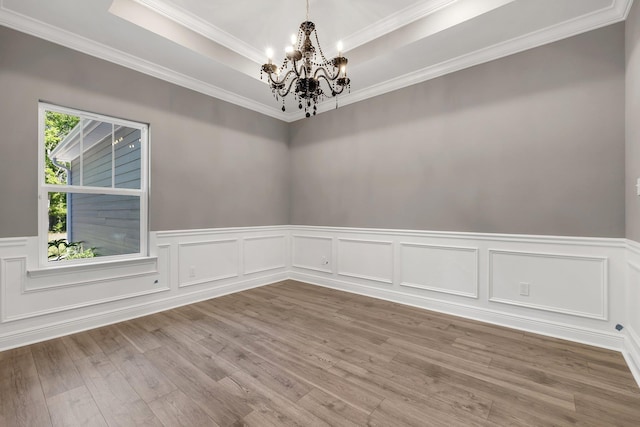 empty room with wainscoting, wood finished floors, a chandelier, and a tray ceiling