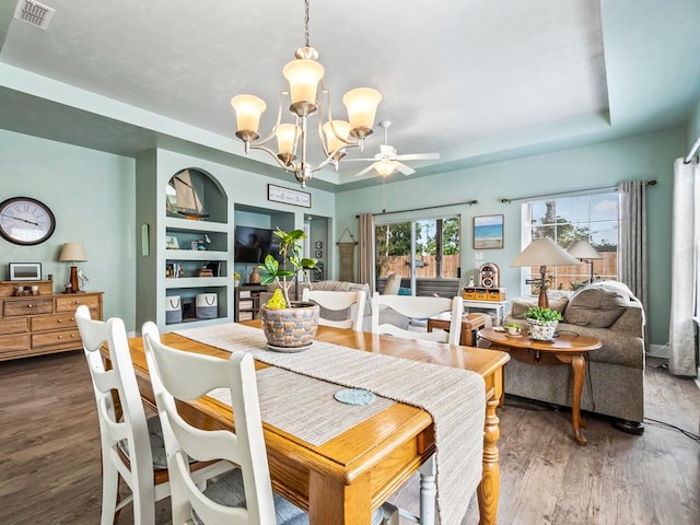 dining space featuring dark wood-type flooring, ceiling fan with notable chandelier, built in features, and a raised ceiling