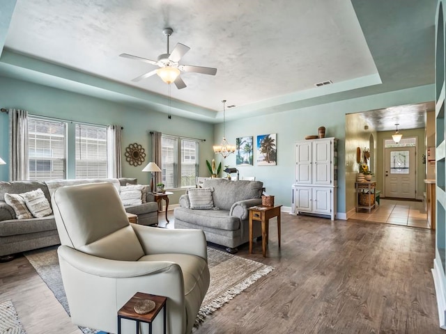 living room featuring ceiling fan with notable chandelier, dark hardwood / wood-style floors, and a tray ceiling