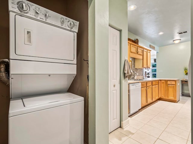 laundry area featuring stacked washer and dryer, light tile patterned floors, and sink