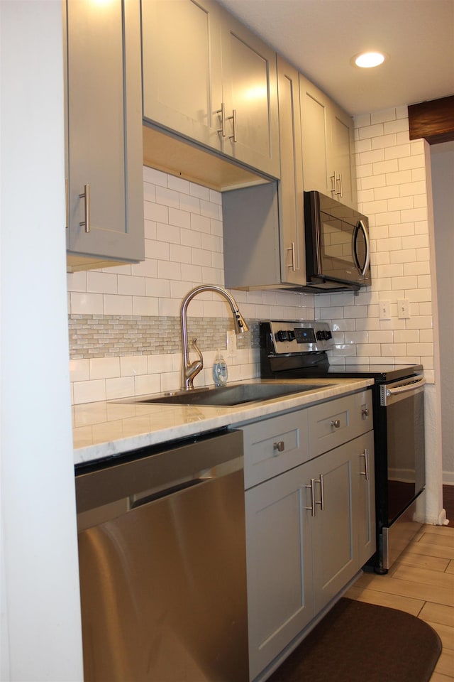 kitchen with tasteful backsplash, gray cabinetry, light hardwood / wood-style floors, and appliances with stainless steel finishes