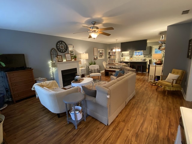 living room featuring ceiling fan with notable chandelier, a fireplace, wood finished floors, and visible vents