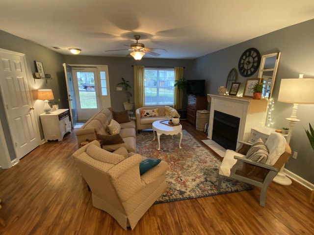 living area featuring baseboards, a fireplace with flush hearth, a ceiling fan, and wood finished floors