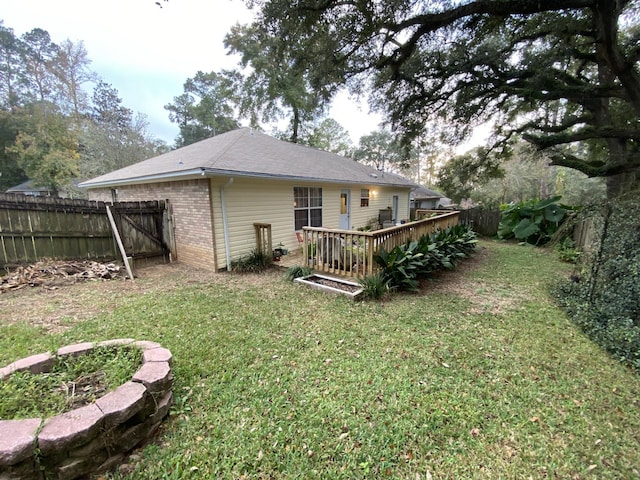 rear view of property featuring a deck, brick siding, a lawn, and a fenced backyard